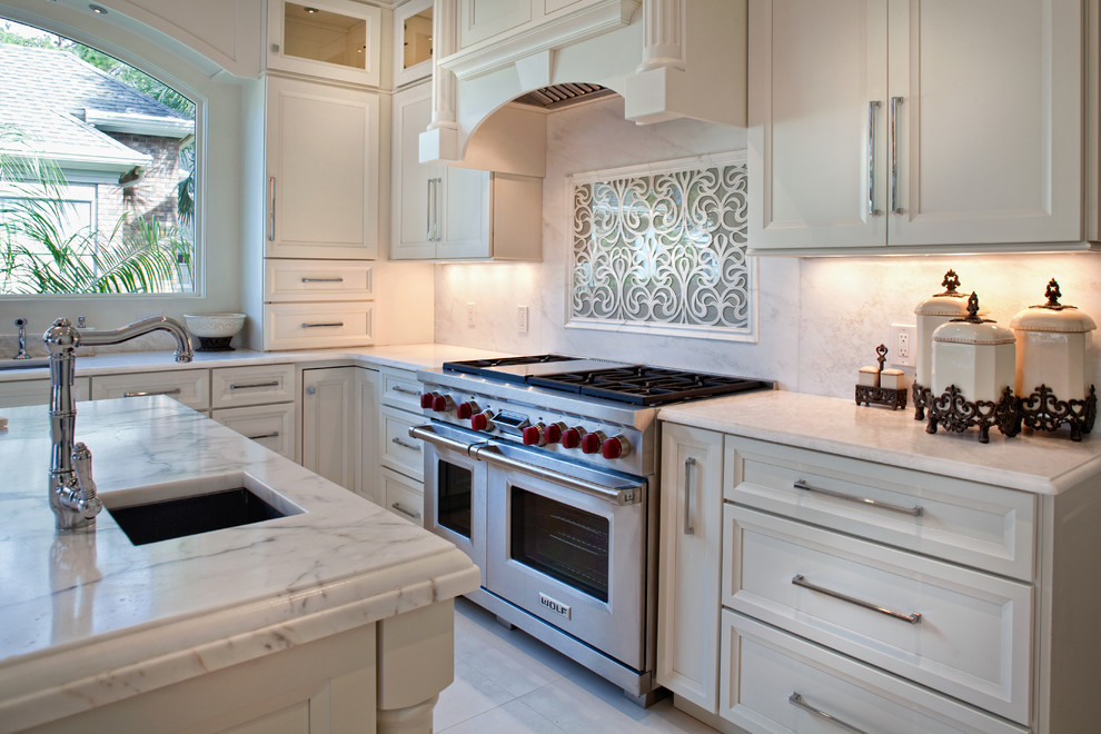 Mid-sized elegant l-shaped ceramic tile eat-in kitchen photo in Charleston with an undermount sink, recessed-panel cabinets, white cabinets, white backsplash, stone tile backsplash, stainless steel appliances and an island