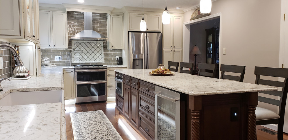 Kitchen - large traditional l-shaped brown floor and dark wood floor kitchen idea in Other with a farmhouse sink, shaker cabinets, white cabinets, quartzite countertops, gray backsplash, porcelain backsplash, stainless steel appliances, an island and gray countertops