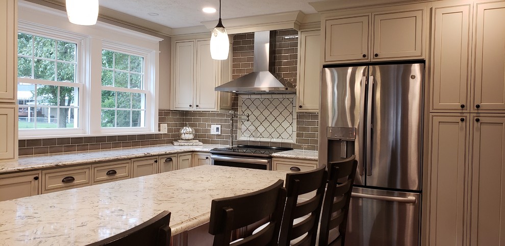 Inredning av ett klassiskt stort grå grått l-kök, med en rustik diskho, skåp i shakerstil, vita skåp, bänkskiva i kvartsit, grått stänkskydd, stänkskydd i porslinskakel, rostfria vitvaror, mörkt trägolv, en köksö och brunt golv