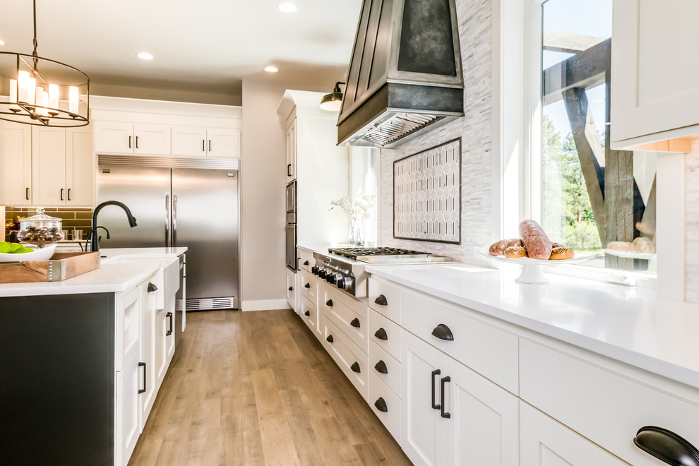 Inspiration for a large farmhouse u-shaped light wood floor and beige floor open concept kitchen remodel in Denver with a farmhouse sink, shaker cabinets, white cabinets, quartz countertops, gray backsplash, marble backsplash, stainless steel appliances, an island and white countertops