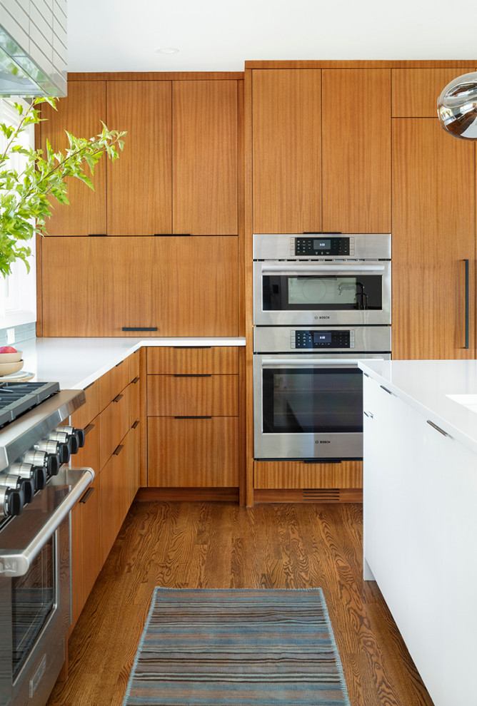 Foto på ett stort 60 tals vit kök, med en undermonterad diskho, släta luckor, skåp i mellenmörkt trä, bänkskiva i kvarts, grått stänkskydd, stänkskydd i keramik, integrerade vitvaror, mellanmörkt trägolv, en köksö och brunt golv