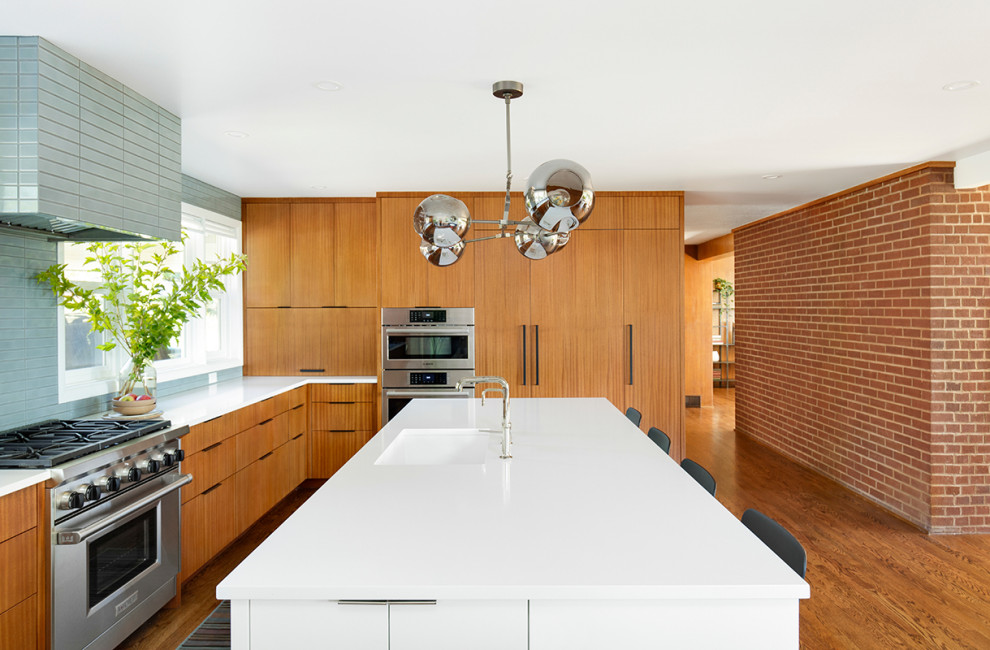 Photo of a large midcentury l-shaped kitchen/diner in Portland with a submerged sink, flat-panel cabinets, medium wood cabinets, engineered stone countertops, grey splashback, ceramic splashback, integrated appliances, medium hardwood flooring, an island, brown floors and white worktops.