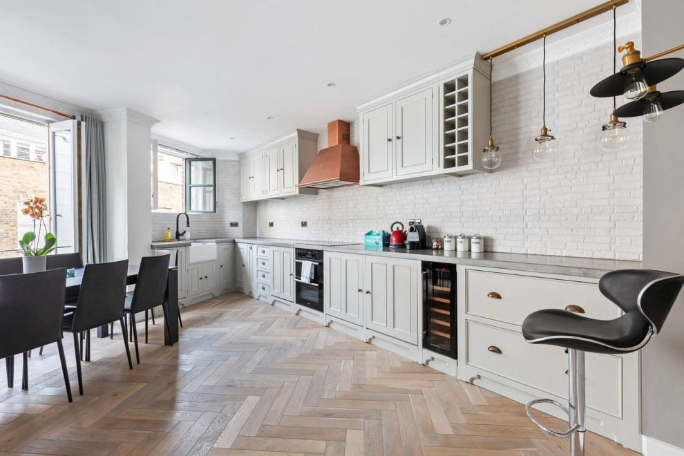 Medium sized urban l-shaped open plan kitchen in London with a belfast sink, shaker cabinets, grey cabinets, concrete worktops, white splashback, porcelain splashback, black appliances, medium hardwood flooring, no island, grey floors and grey worktops.