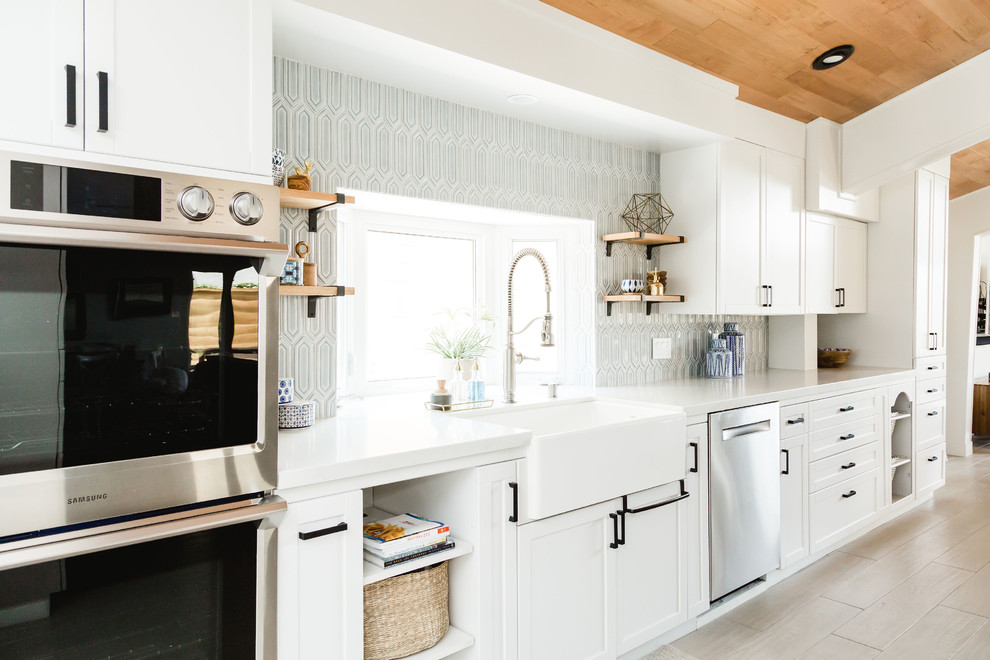 Eat-in kitchen - large coastal l-shaped porcelain tile and brown floor eat-in kitchen idea in San Diego with a farmhouse sink, shaker cabinets, black cabinets, quartz countertops, blue backsplash, ceramic backsplash, stainless steel appliances, a peninsula and white countertops