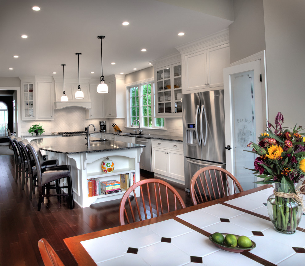Eat-in kitchen - large traditional l-shaped dark wood floor and brown floor eat-in kitchen idea in Philadelphia with an undermount sink, shaker cabinets, white cabinets, granite countertops, white backsplash, subway tile backsplash, stainless steel appliances and an island