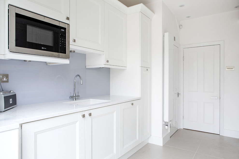 Photo of a small traditional galley enclosed kitchen in London with white cabinets, blue splashback, no island, a submerged sink, shaker cabinets, quartz worktops, glass sheet splashback and black appliances.
