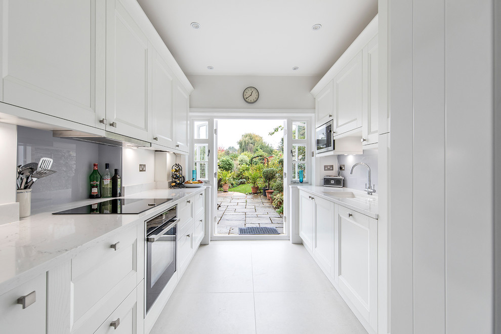 Small traditional galley enclosed kitchen in London with white cabinets, no island, a submerged sink, glass sheet splashback, black appliances, white floors, white worktops, shaker cabinets, quartz worktops and blue splashback.