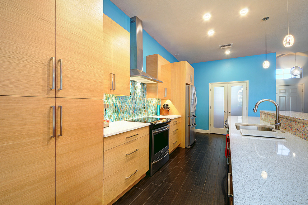Bild på ett stort funkis kök, med en enkel diskho, släta luckor, skåp i ljust trä, bänkskiva i kvarts, blått stänkskydd, stänkskydd i glaskakel, rostfria vitvaror, klinkergolv i porslin och en köksö