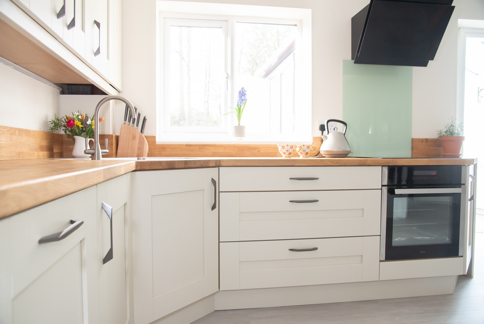 Inspiration for a large contemporary kitchen/diner in Sussex with shaker cabinets, white cabinets, wood worktops, black appliances, laminate floors and no island.