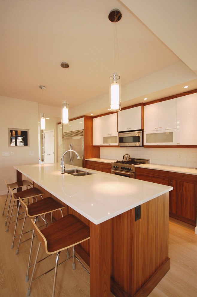 Immagine di una cucina parallela minimal con lavello a doppia vasca, ante lisce, ante bianche, elettrodomestici in acciaio inossidabile e parquet chiaro