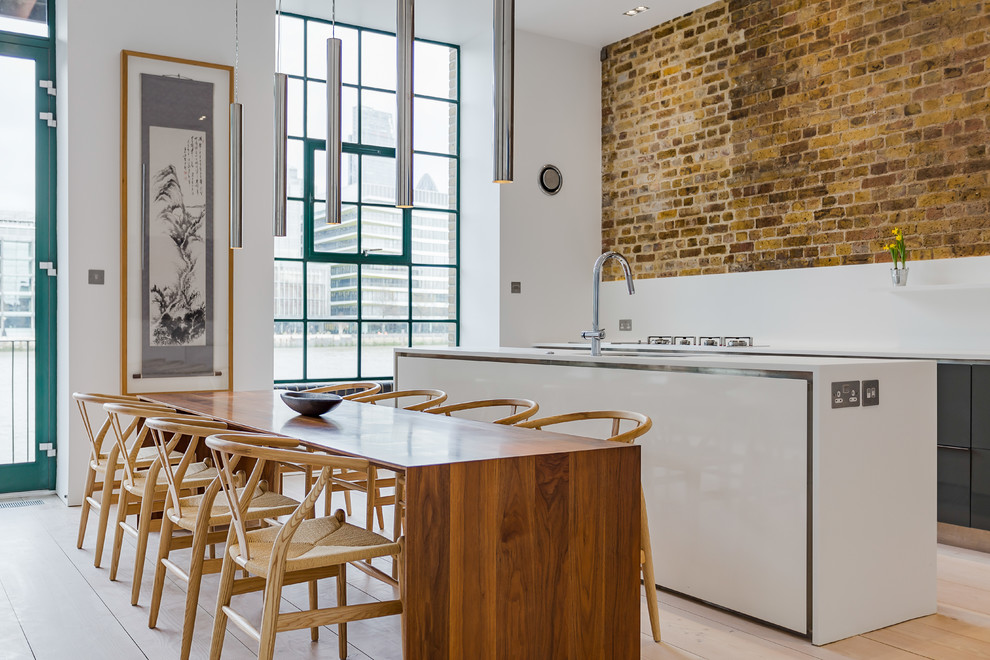 На фото: параллельная кухня-гостиная в стиле лофт с плоскими фасадами, серыми фасадами, белым фартуком, полом из ламината, островом и бежевым полом