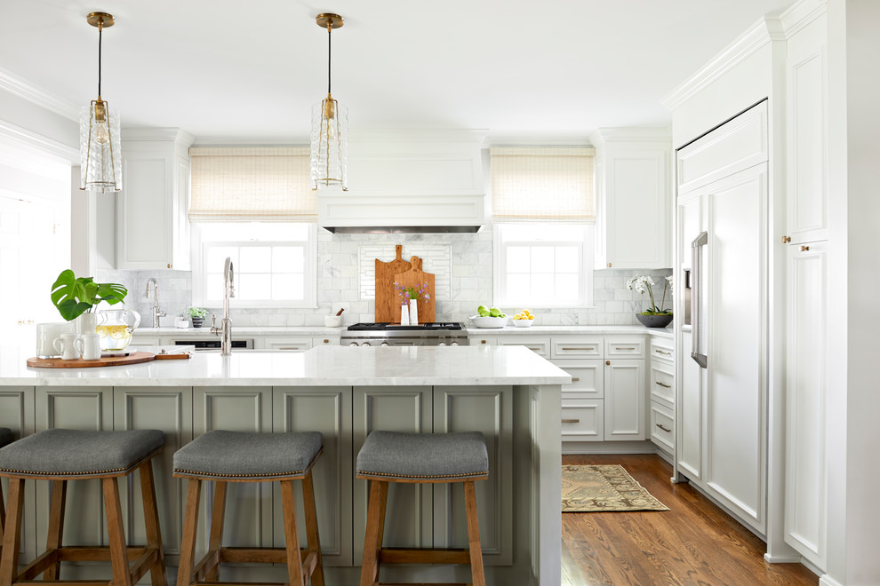 This is an example of a large traditional l-shaped kitchen/diner in Nashville with a belfast sink, white splashback, marble splashback, an island, recessed-panel cabinets, white cabinets, integrated appliances, medium hardwood flooring and brown floors.