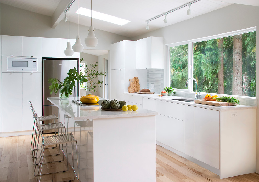 This is an example of a medium sized contemporary kitchen in Vancouver with a single-bowl sink, flat-panel cabinets, white cabinets, grey splashback, stainless steel appliances, light hardwood flooring and an island.