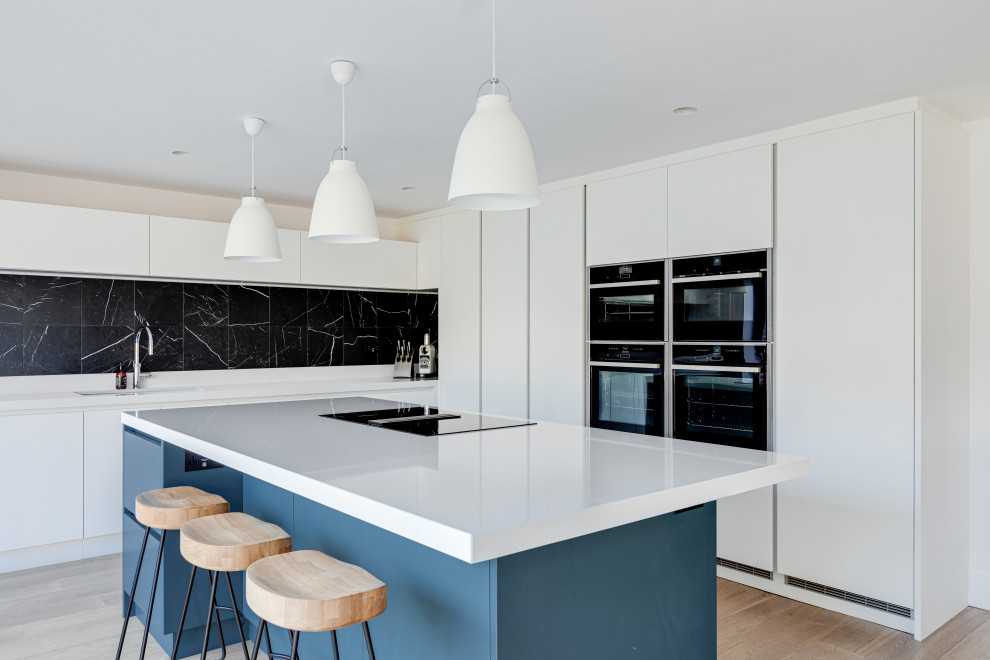 Inspiration for an expansive contemporary u-shaped kitchen/diner in Hertfordshire with an integrated sink, flat-panel cabinets, white cabinets, quartz worktops, black splashback, metal splashback, black appliances, painted wood flooring, an island, white floors and white worktops.