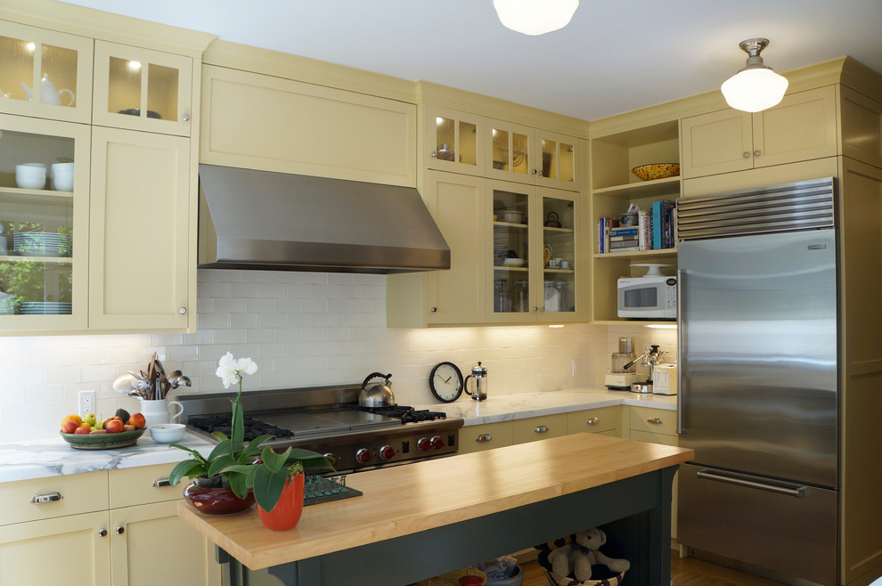 Offene Klassische Küche in U-Form mit integriertem Waschbecken, Schrankfronten im Shaker-Stil, gelben Schränken, Marmor-Arbeitsplatte, Küchenrückwand in Weiß, Rückwand aus Keramikfliesen, Küchengeräten aus Edelstahl, braunem Holzboden und zwei Kücheninseln in San Francisco