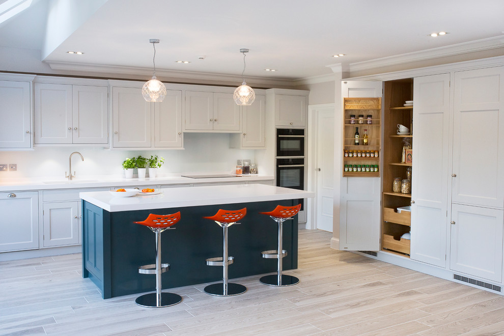 Klassische Küche mit Schrankfronten im Shaker-Stil, beigen Schränken, Küchenrückwand in Weiß, schwarzen Elektrogeräten, hellem Holzboden und Kücheninsel in Kent
