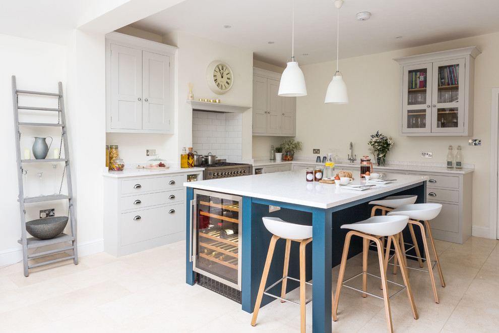 Photo of a large traditional l-shaped open plan kitchen in London with shaker cabinets, white cabinets, engineered stone countertops, white splashback, metro tiled splashback, stainless steel appliances, an island, beige floors and a double-bowl sink.