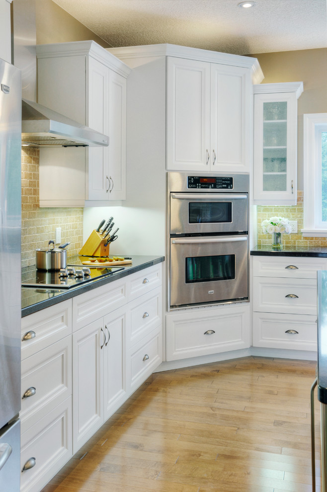 Example of a mid-sized trendy l-shaped medium tone wood floor eat-in kitchen design in Other with an undermount sink, shaker cabinets, white cabinets, granite countertops, beige backsplash, stone tile backsplash, stainless steel appliances and an island