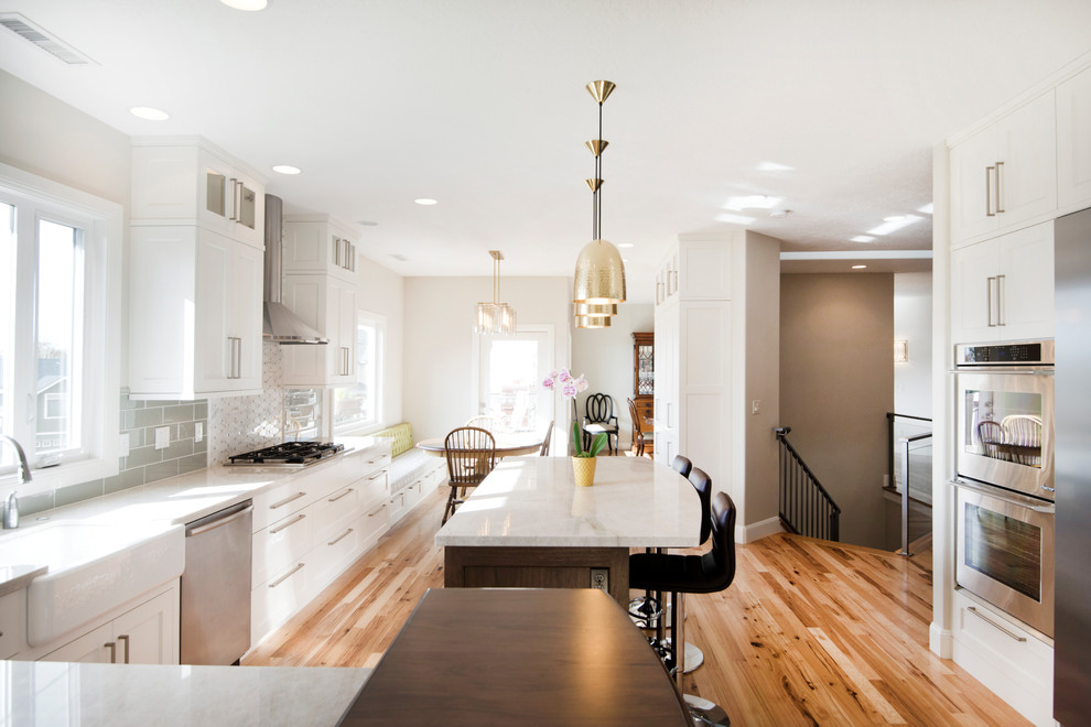 Modern inredning av ett mellanstort vit vitt kök, med en rustik diskho, skåp i shakerstil, vita skåp, bänkskiva i kvarts, grönt stänkskydd, stänkskydd i keramik, rostfria vitvaror, mellanmörkt trägolv, en köksö och brunt golv