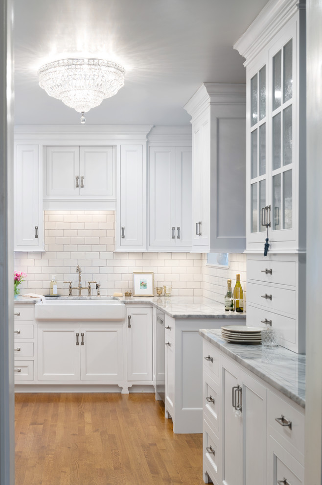 Inspiration for a cottage medium tone wood floor kitchen remodel in Cincinnati with a farmhouse sink, white cabinets, marble countertops, white backsplash, ceramic backsplash and stainless steel appliances