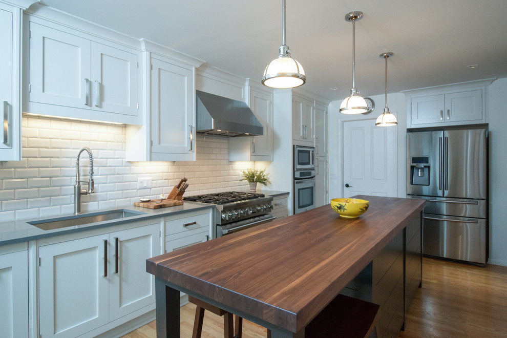 Eat-in kitchen - mid-sized contemporary galley light wood floor eat-in kitchen idea in Detroit with an undermount sink, shaker cabinets, quartz countertops, white backsplash, ceramic backsplash, stainless steel appliances and an island