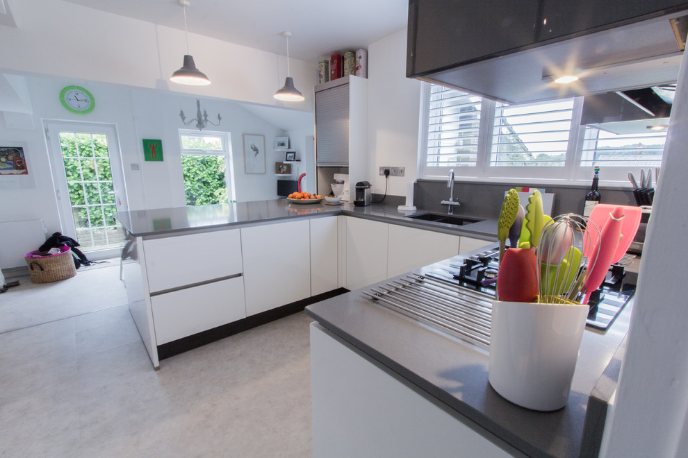 Foto på ett mellanstort funkis kök, med en undermonterad diskho, släta luckor, vita skåp, bänkskiva i kvartsit, grått stänkskydd, stänkskydd i sten, rostfria vitvaror och klinkergolv i keramik