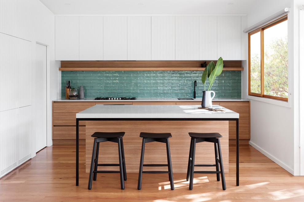 Idées déco pour une cuisine linéaire contemporaine en bois brun avec un placard à porte plane, une crédence bleue, un sol en bois brun, îlot, un sol marron et un plan de travail blanc.