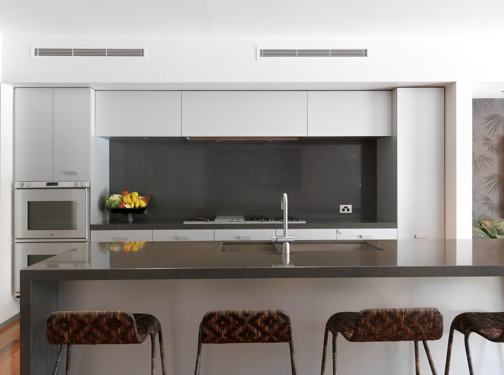 Источник вдохновения для домашнего уюта: параллельная кухня в современном стиле с двойной мойкой, плоскими фасадами, белыми фасадами, черным фартуком, фартуком из стекла и обоями на стенах
