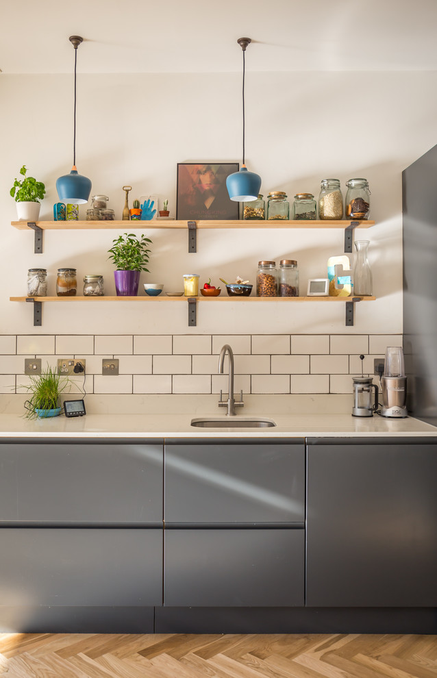 Modern inredning av ett kök, med en undermonterad diskho, släta luckor, grå skåp, vitt stänkskydd, stänkskydd i tunnelbanekakel, ljust trägolv och brunt golv