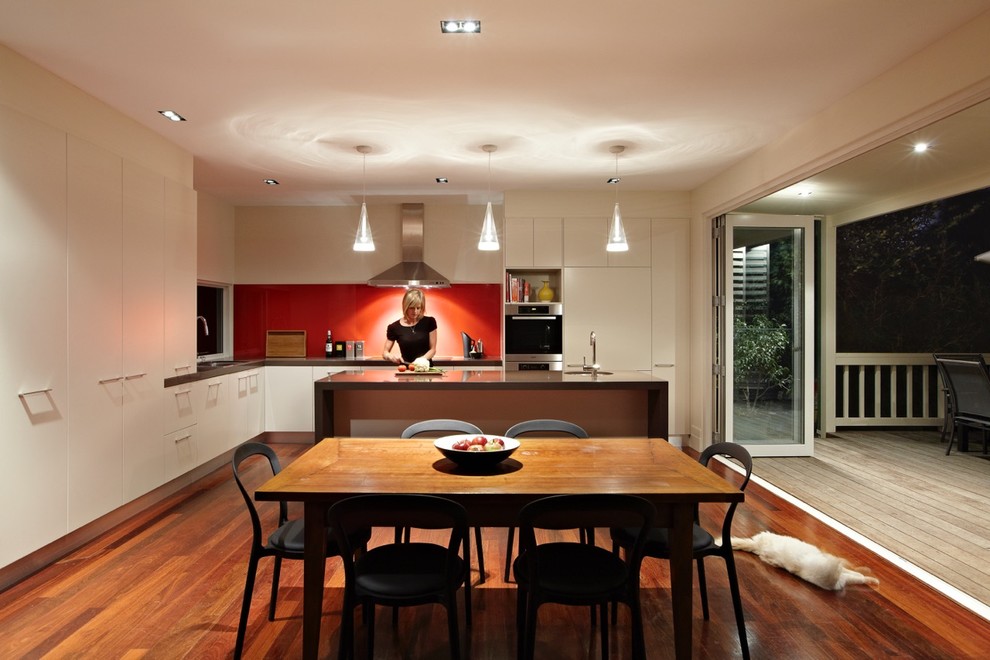 Mittelgroße Moderne Wohnküche mit weißen Schränken, Küchenrückwand in Rot, braunem Holzboden, Kücheninsel, Quarzwerkstein-Arbeitsplatte und Glasrückwand in Melbourne