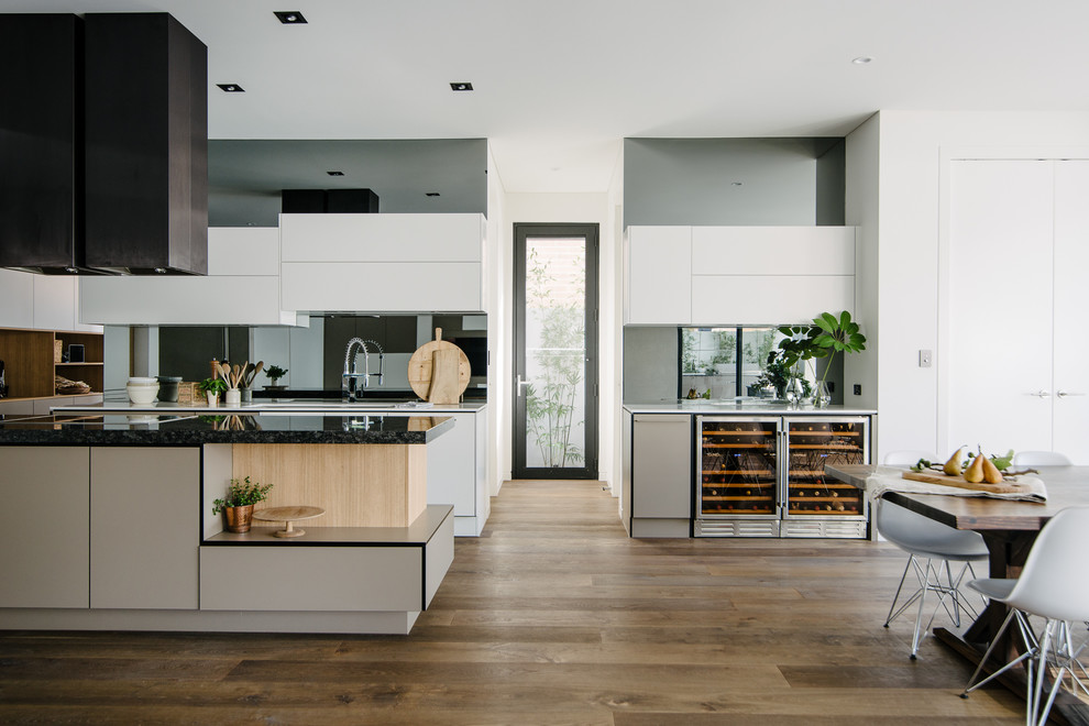 Inredning av ett modernt mellanstort kök, med en undermonterad diskho, granitbänkskiva, svart stänkskydd, spegel som stänkskydd, rostfria vitvaror, mörkt trägolv och en köksö