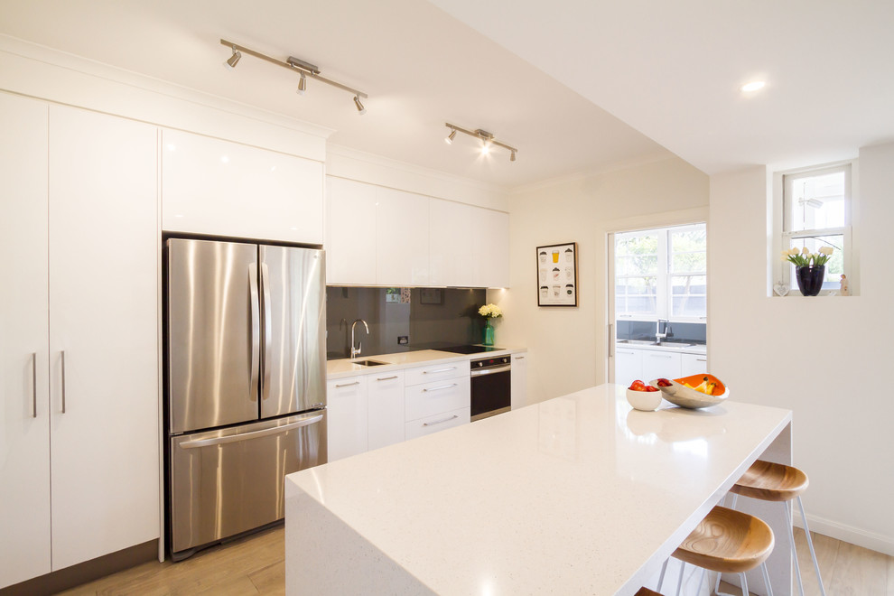 Zweizeilige, Mittelgroße Moderne Wohnküche mit flächenbündigen Schrankfronten, weißen Schränken, Quarzwerkstein-Arbeitsplatte, Küchenrückwand in Grau, Glasrückwand, Küchengeräten aus Edelstahl, hellem Holzboden und Kücheninsel in Melbourne