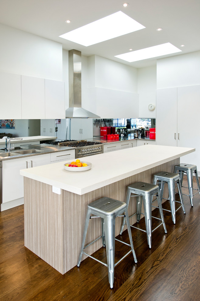 Foto på ett stort funkis kök, med en dubbel diskho, släta luckor, vita skåp, stänkskydd med metallisk yta, mörkt trägolv, bänkskiva i rostfritt stål, spegel som stänkskydd, rostfria vitvaror och en köksö