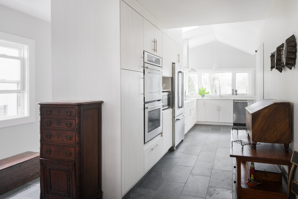 Inredning av ett modernt mellanstort kök, med en dubbel diskho, släta luckor, vita skåp, marmorbänkskiva, vitt stänkskydd, stänkskydd i marmor, rostfria vitvaror, skiffergolv och svart golv
