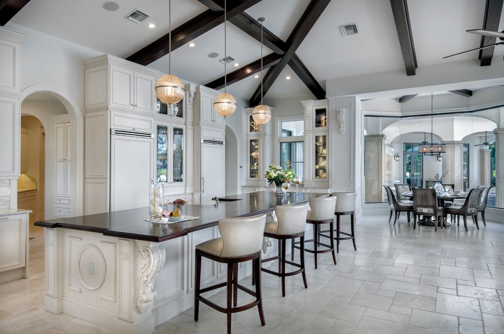Inspiration for a large mediterranean l-shaped travertine floor and beige floor eat-in kitchen remodel in Miami with a farmhouse sink, raised-panel cabinets, gray cabinets, granite countertops, mosaic tile backsplash, paneled appliances and an island