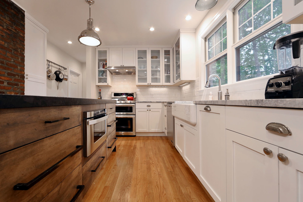 Example of a large eclectic l-shaped light wood floor kitchen design in Boston with an undermount sink, shaker cabinets, white cabinets, granite countertops, white backsplash, subway tile backsplash, stainless steel appliances and an island
