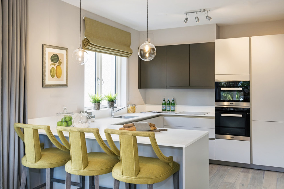 Contemporary u-shaped kitchen in Dublin with a single-bowl sink, flat-panel cabinets, white cabinets, grey splashback, black appliances, a breakfast bar and white worktops.