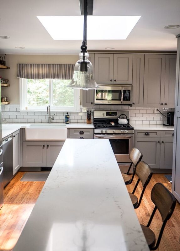 Inspiration for a large transitional light wood floor and brown floor eat-in kitchen remodel in New York with a farmhouse sink, recessed-panel cabinets, gray cabinets, marble countertops, white backsplash, subway tile backsplash, stainless steel appliances and an island