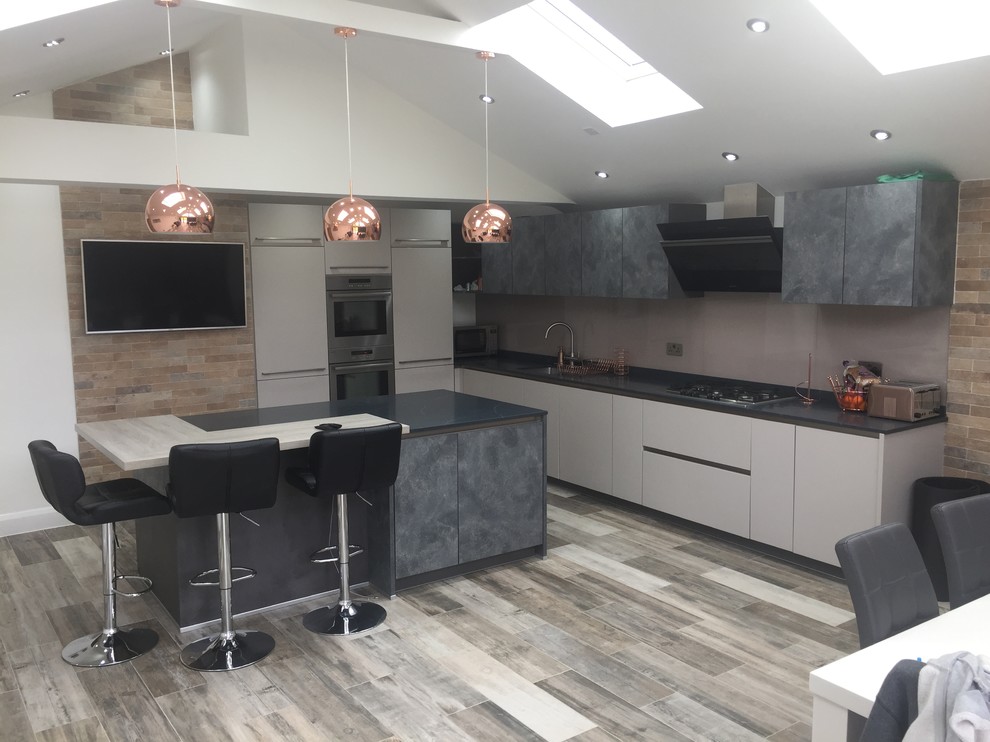 Inspiration for a medium sized contemporary l-shaped kitchen/diner in Berkshire with flat-panel cabinets, quartz worktops, glass sheet splashback, an island and black worktops.