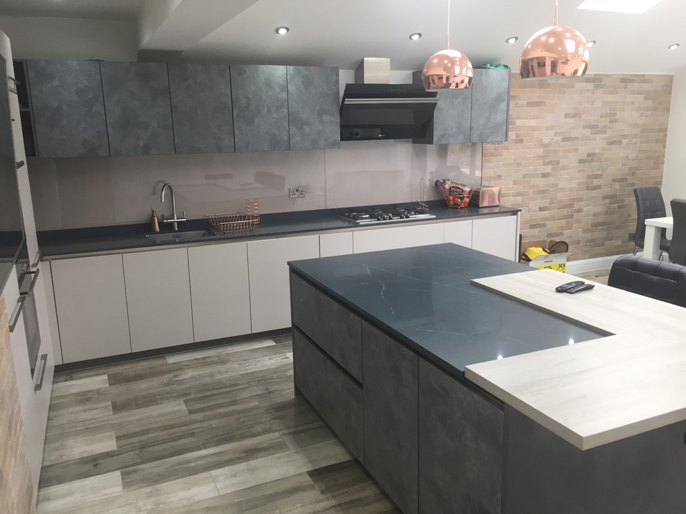 This is an example of a medium sized contemporary l-shaped kitchen/diner in Berkshire with flat-panel cabinets, quartz worktops, glass sheet splashback, an island and black worktops.