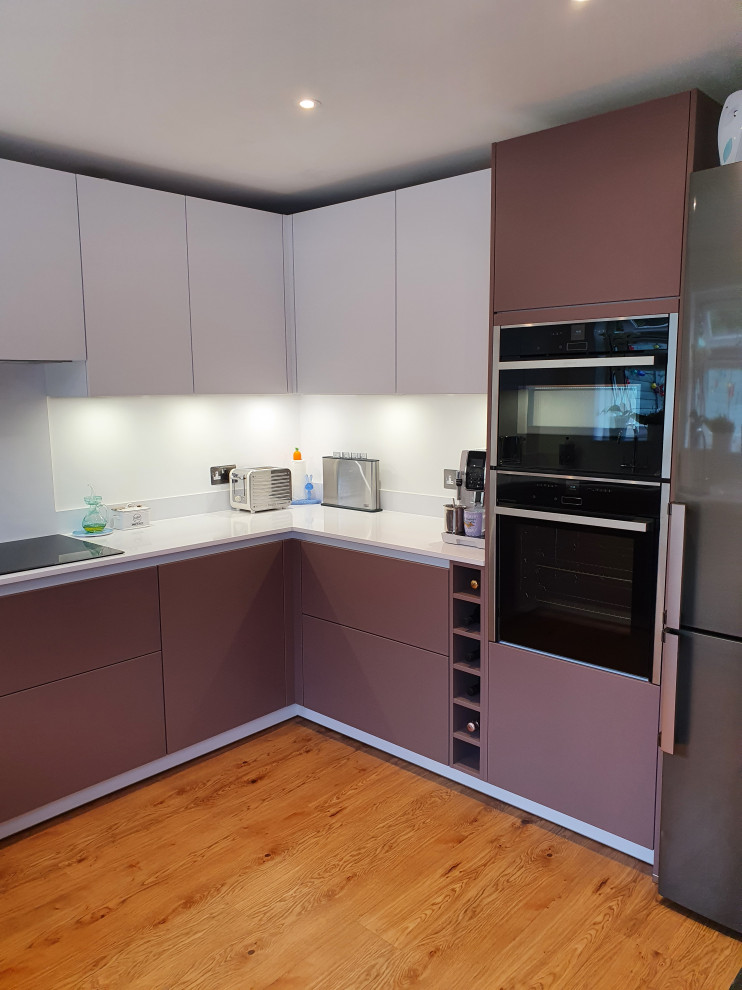This is an example of a medium sized contemporary u-shaped kitchen/diner in Berkshire with flat-panel cabinets, quartz worktops, white splashback, stone slab splashback, black appliances, no island and white worktops.
