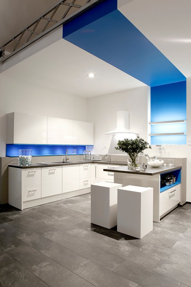 Mittelgroße Moderne Küche in U-Form mit integriertem Waschbecken, weißen Schränken, Laminat-Arbeitsplatte, Küchenrückwand in Blau, Rückwand aus Steinfliesen, weißen Elektrogeräten und dunklem Holzboden in Sonstige