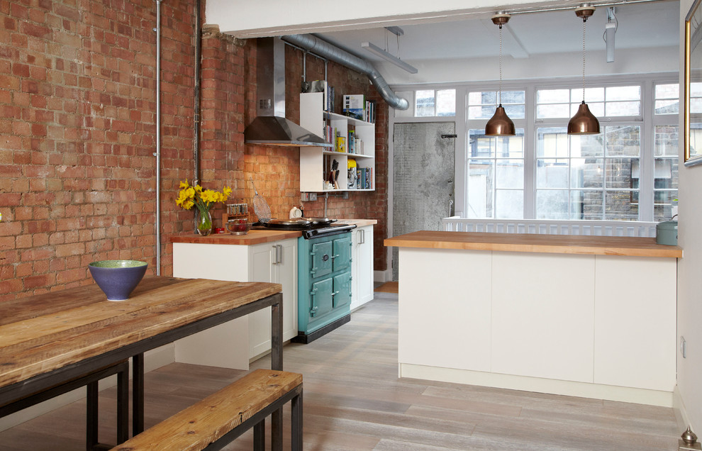 This is an example of a medium sized industrial kitchen/diner in London with a belfast sink, shaker cabinets, white cabinets, wood worktops, stainless steel appliances, medium hardwood flooring and a breakfast bar.