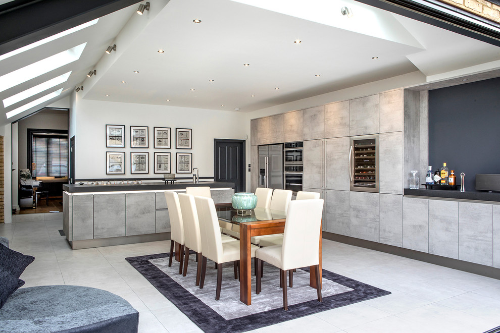 Example of a large trendy l-shaped gray floor eat-in kitchen design in London with flat-panel cabinets, distressed cabinets, stainless steel appliances, an island, black countertops and granite countertops