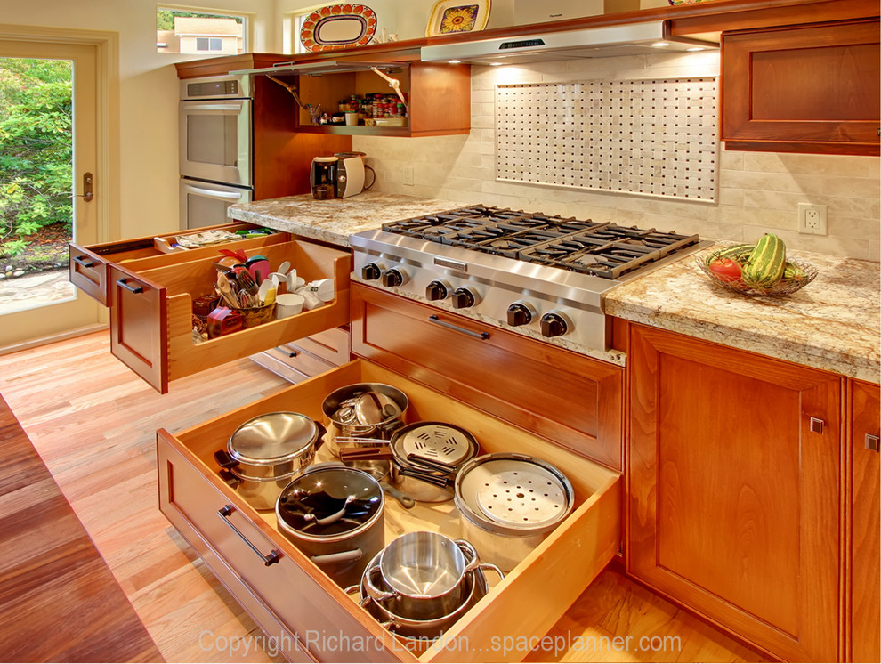 Klassisk inredning av ett stort kök och matrum, med en undermonterad diskho, skåp i ljust trä, granitbänkskiva, rostfria vitvaror, ljust trägolv och en köksö