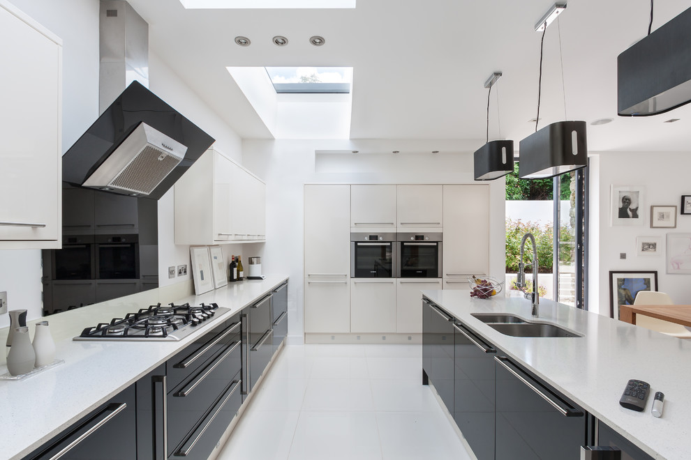 Photo of an expansive contemporary kitchen/diner in Other with a double-bowl sink, flat-panel cabinets, black cabinets, black splashback, glass sheet splashback, stainless steel appliances, an island, white floors and white worktops.