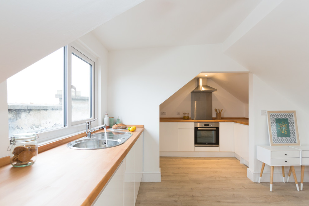 Contemporary u-shaped open plan kitchen in London with a built-in sink, flat-panel cabinets, white cabinets, wood worktops, window splashback, stainless steel appliances, brown floors, brown worktops and light hardwood flooring.
