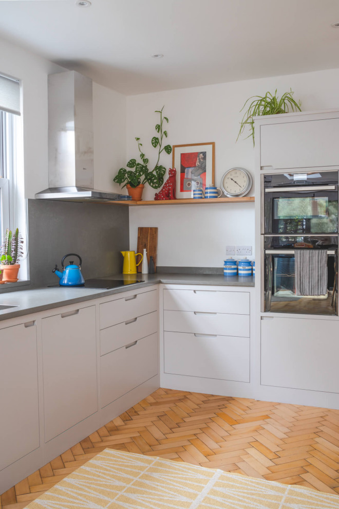 Modern inredning av ett litet grå grått l-kök, med släta luckor, grå skåp, bänkskiva i kvartsit, ljust trägolv, en undermonterad diskho och beiget golv