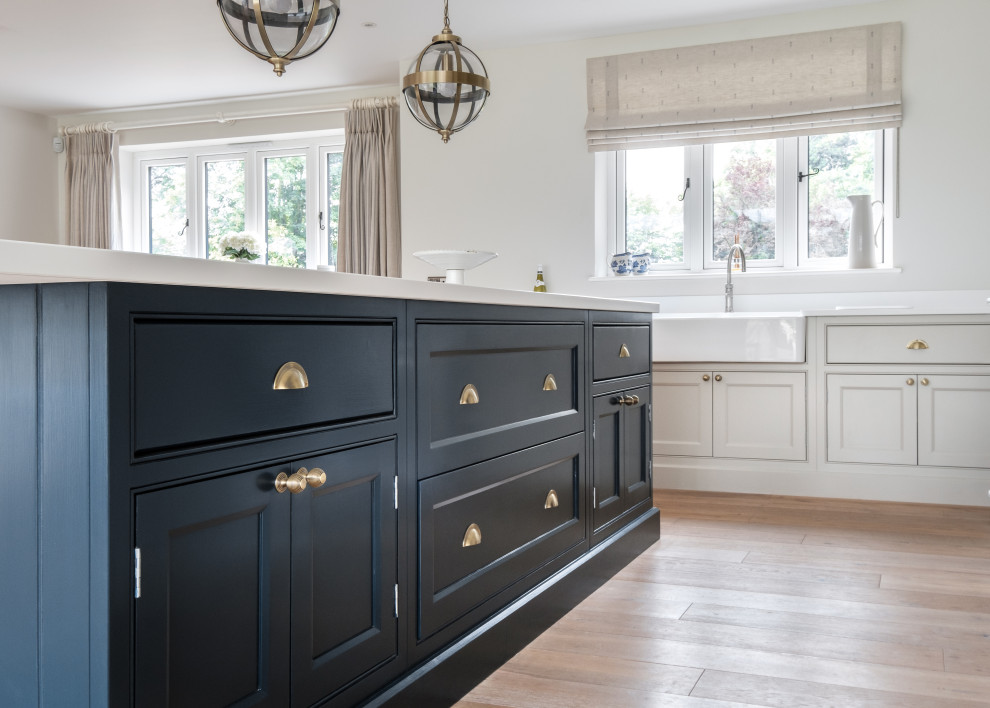 Inspiration for a transitional light wood floor and brown floor kitchen remodel in Gloucestershire with a farmhouse sink, beaded inset cabinets, blue cabinets, white backsplash, quartz backsplash, paneled appliances and white countertops