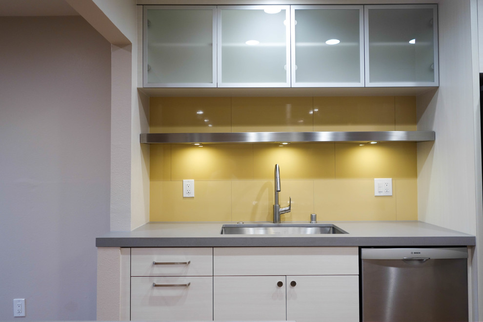 This is an example of a small contemporary galley kitchen/diner in San Francisco with a single-bowl sink, flat-panel cabinets, beige cabinets, engineered stone countertops, yellow splashback, porcelain splashback, stainless steel appliances, cork flooring, yellow floors and grey worktops.